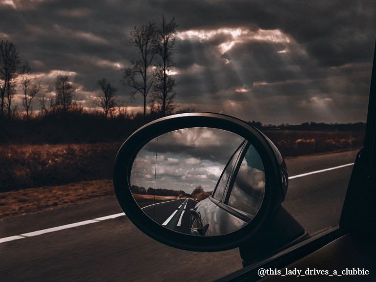  MINI Cooper mirror view on the road in an autumn landscape.